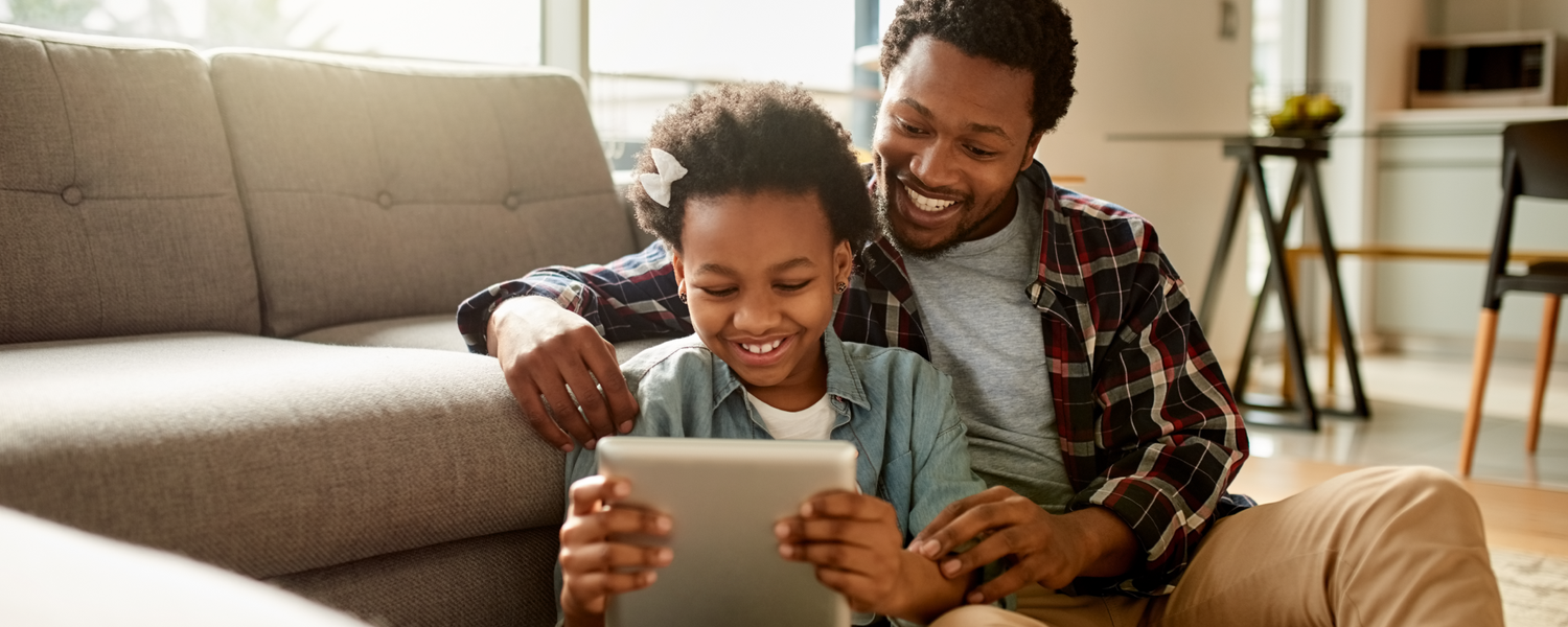 father and daughter sitting on floor in front of couch using anywhere teacher on a tablet