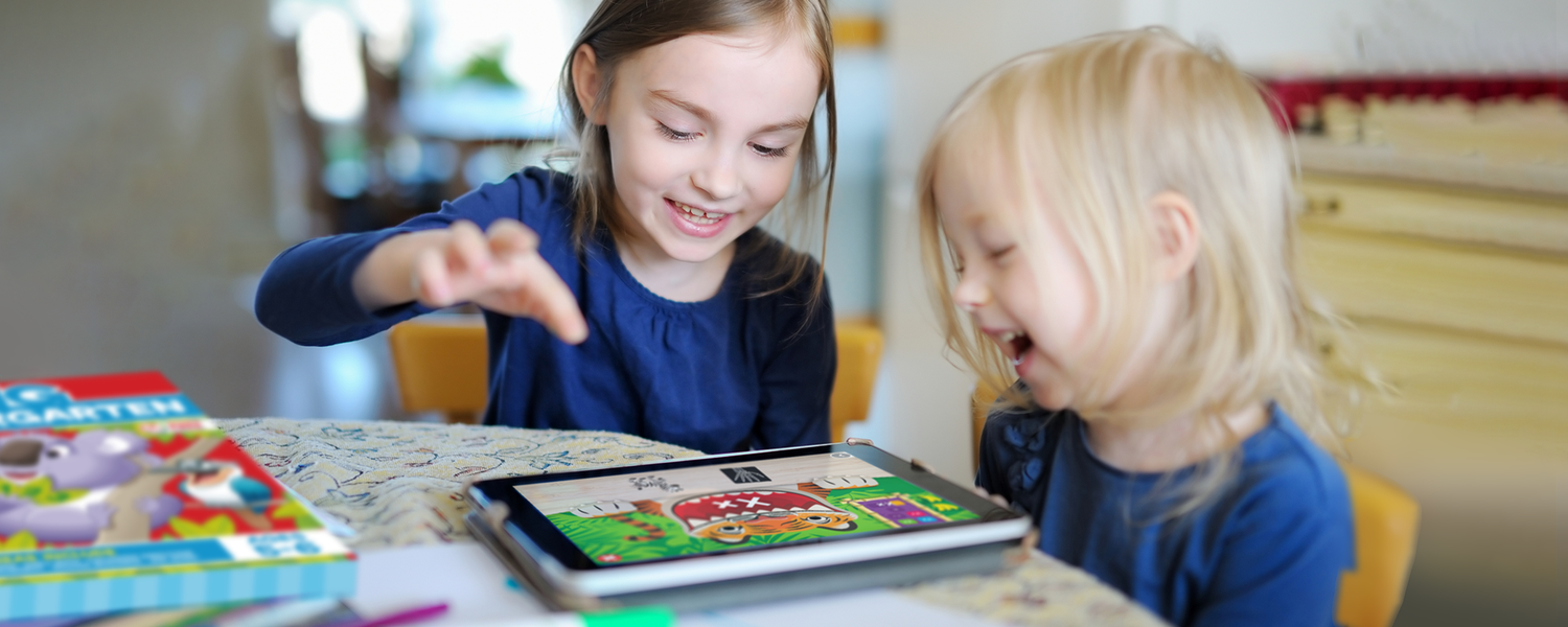 two sisters laughing and having fun playing anywhere teacher on a tablet on kitchen table