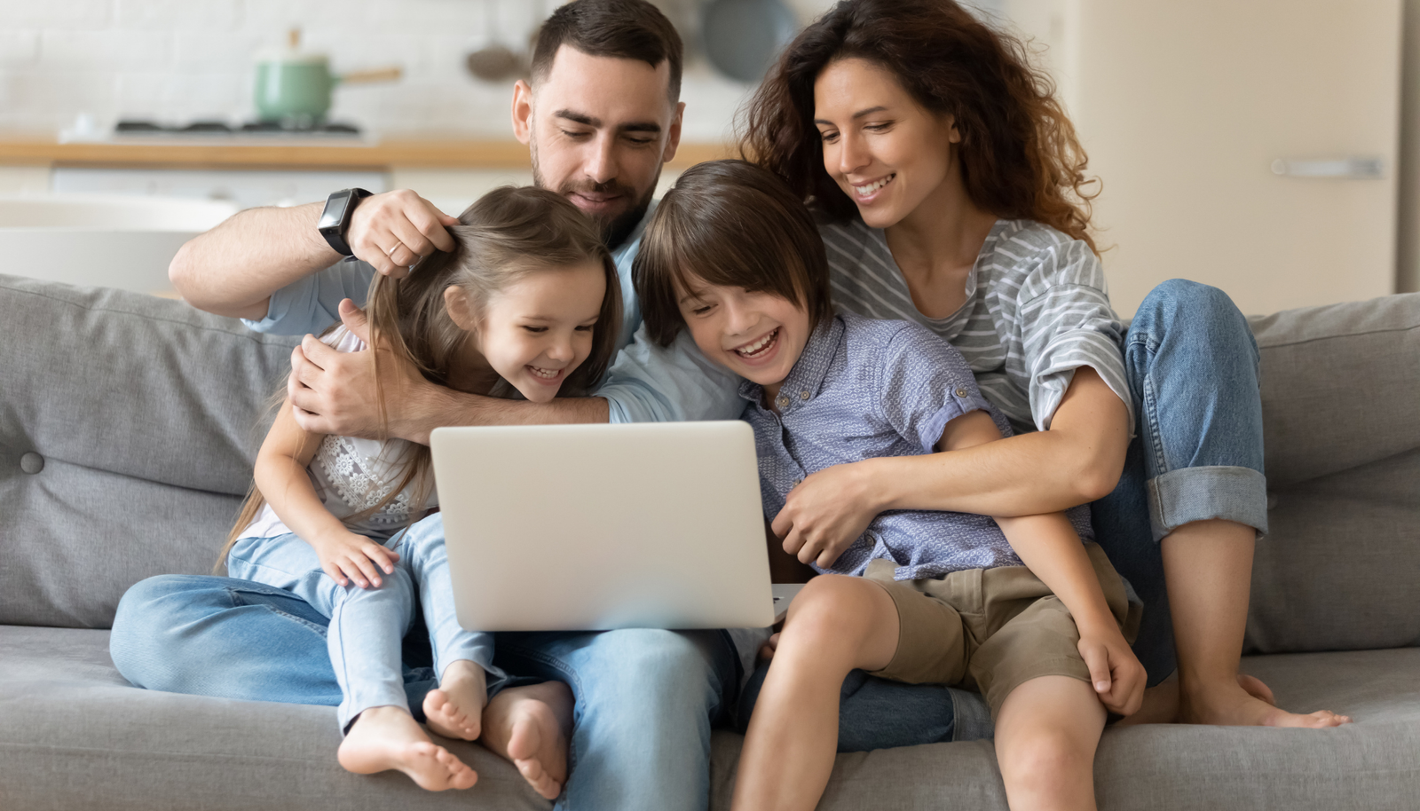 a dad, mom, young son and daughter sitting together on a couch enjoying time together doing something on a laptop