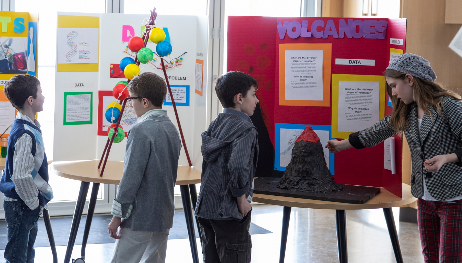 kids at a science fair showing and telling about their science fair projects of a volcano, and a DNA chain